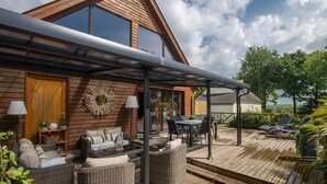 A wooden house with a covered patio, outdoor furniture, and a view of the surrounding landscape. - "Chambre Belle Époque" Guest Room with Shared Terrace, Garden & Wi-Fi (Guerlédan)