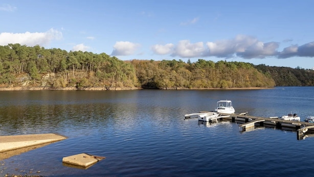 A calm lake with a dock and boats, surrounded by a forested shoreline. - "Chambre Belle Époque" Guest Room with Shared Terrace, Garden & Wi-Fi (Guerlédan)