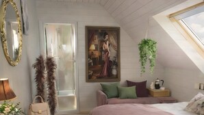 A bedroom with a sloped ceiling, a bed with a green blanket, a painting on the wall, a hanging plant, and a suitcase on a dresser. - "Chambre Belle Époque" Guest Room with Shared Terrace, Garden & Wi-Fi (Guerlédan)