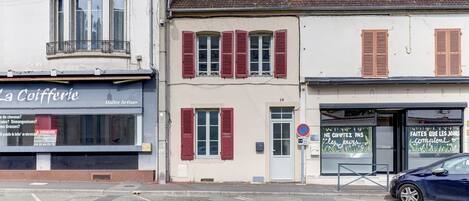 A street view with a café named 'La Cofferie' on the left, a building with red shutters in the middle, and a blue car parked on the right.