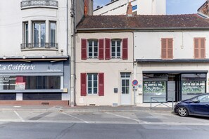 A street view with a café named 'La Cofferie' on the left, a building with red shutters in the middle, and a blue car parked on the right. - Le Cocon Bleu - Bel appt pour 6 en centre-ville (Montlucon)
