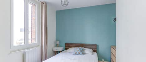 Une chambre à coucher avec un lit, une table de chevet, une lampe, une fenêtre et un luminaire suspendu.