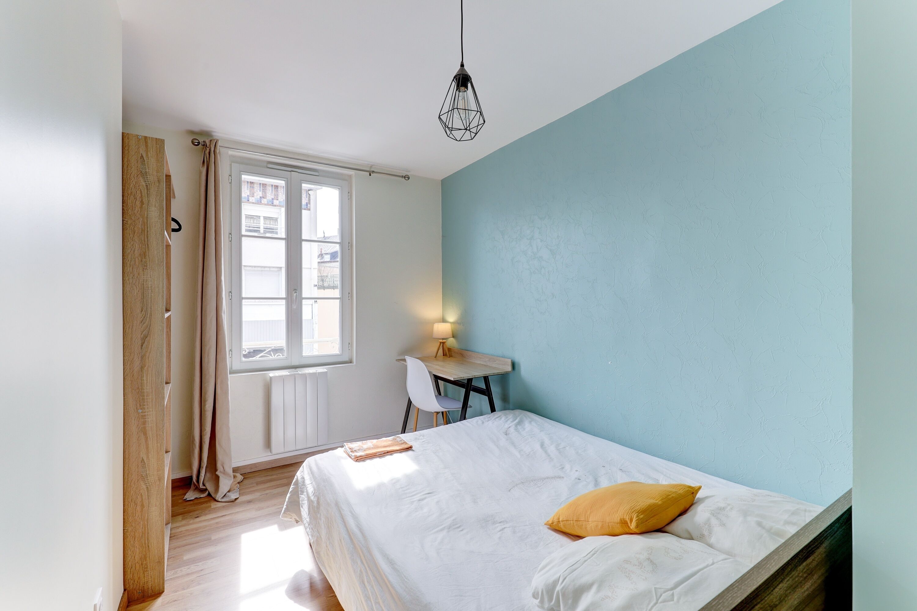 Ein Schlafzimmer mit Bett, Schreibtisch, Stuhl, Fenster und Heizkörper.