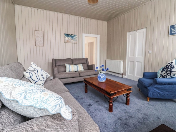 A living room with a sofa, a blue armchair, a wooden coffee table, and a vase with flowers.