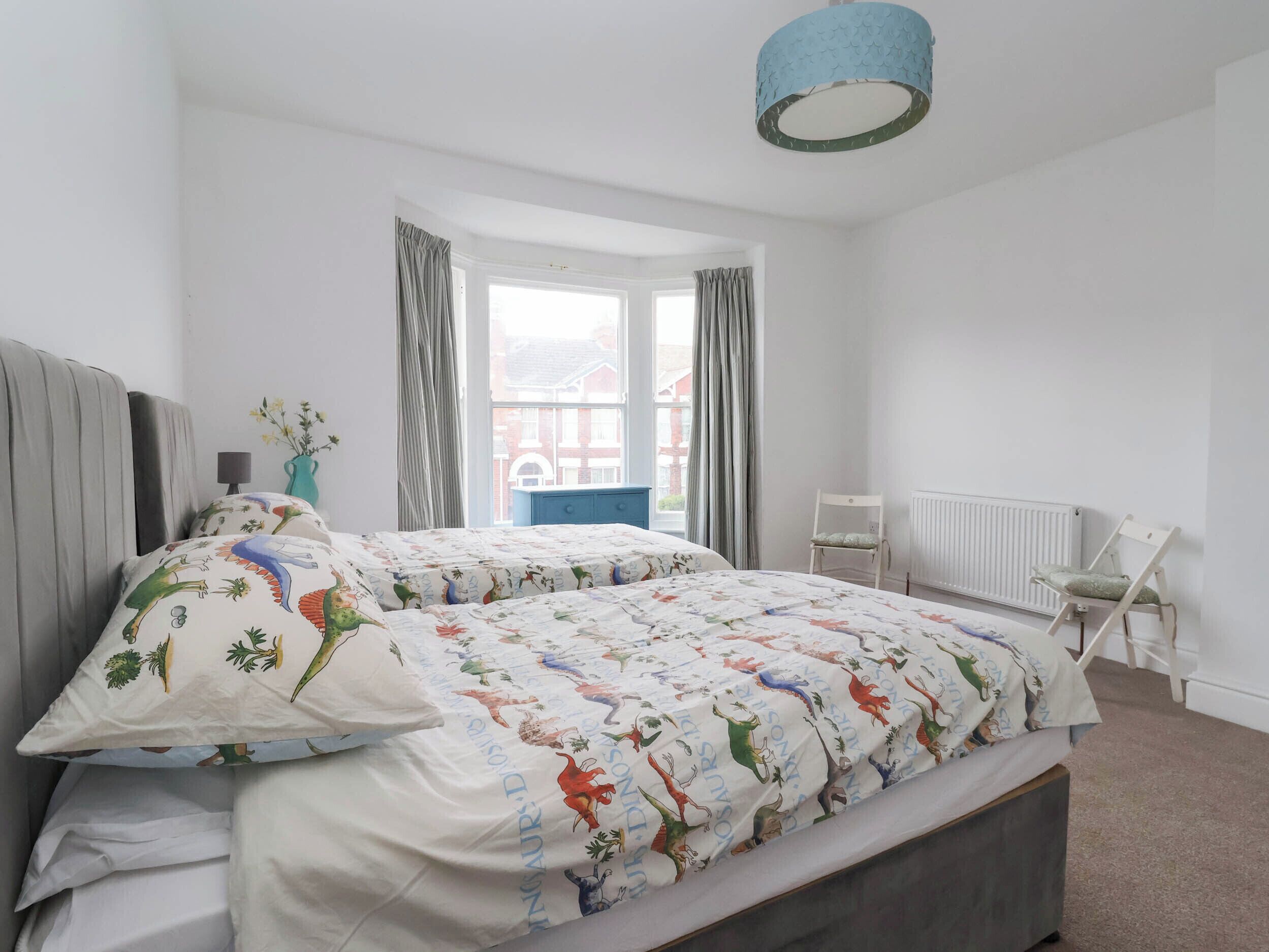 A bedroom with a bed, a window, curtains, a radiator, and a chair.