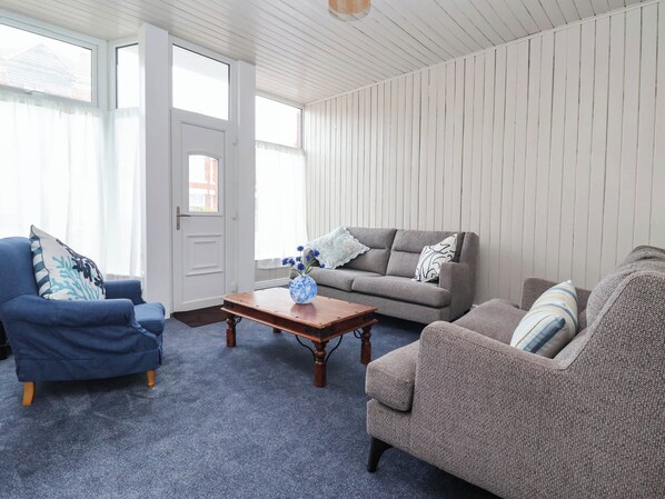 A living room with a blue armchair, a grey sofa, and a brown armchair. There is a wooden coffee table with a vase of flowers.