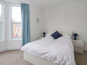 A bedroom with a bed, two bedside tables, a window with curtains, and a view of buildings outside.