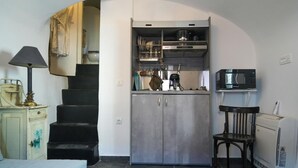 Uma cozinha compacta com fogão embutido, micro-ondas e um pequeno espaço de refeições com uma cadeira.