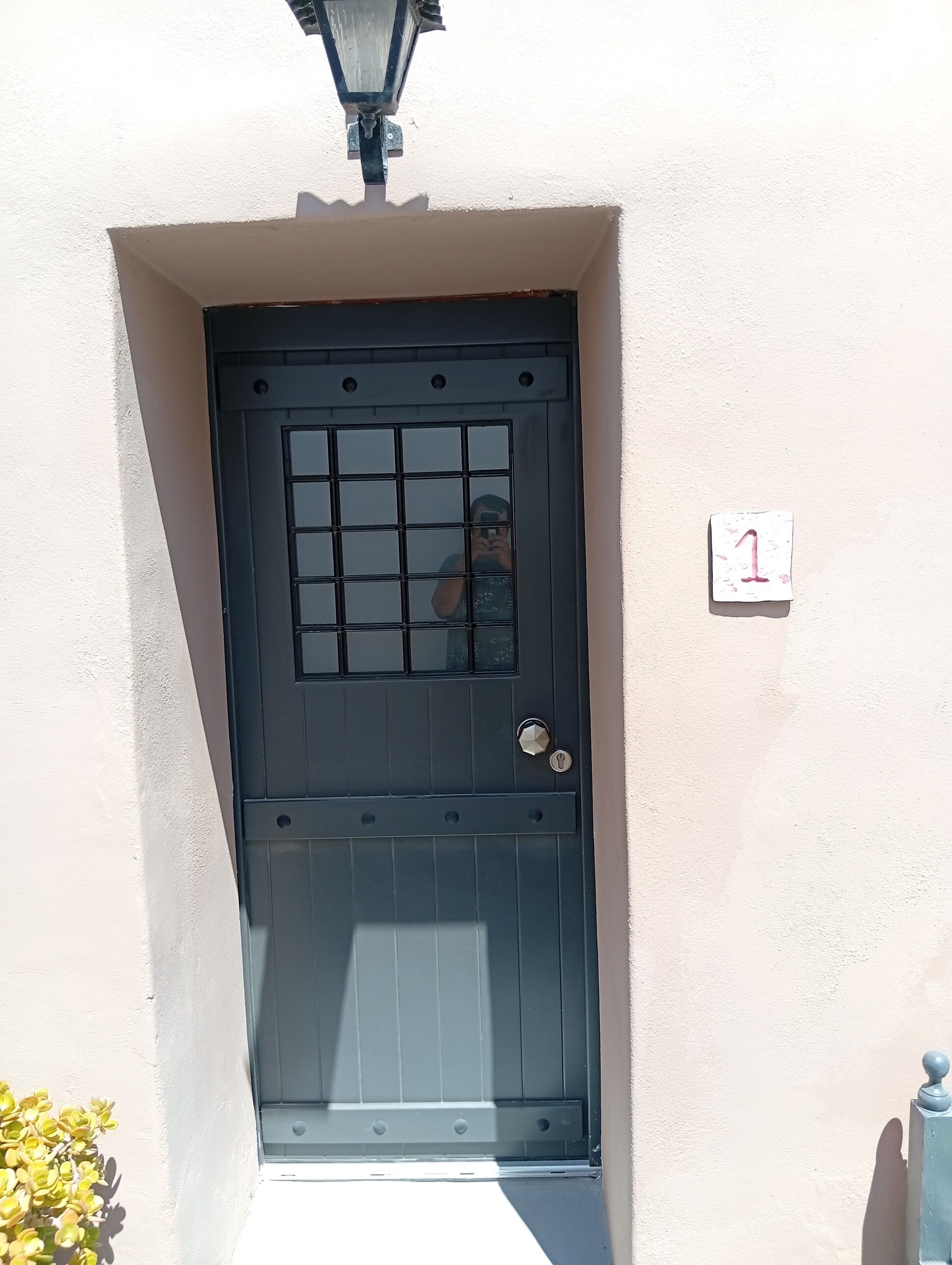 Una puerta negra con un diseño de cuadrícula, una cerradura y una pequeña señal de número en la pared de al lado.
