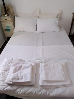 Una cama bien hecha con sábanas blancas y dos toallas dobladas.