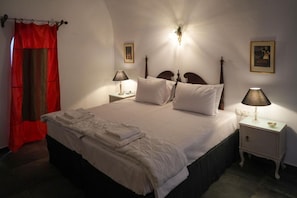 A neatly made bed with pillows and a folded towel, a bedside lamp, a framed picture on the wall, and a red curtain. - Apartment 'Two-Bedroom' with Wi-Fi and Air Conditioning (Emporio)