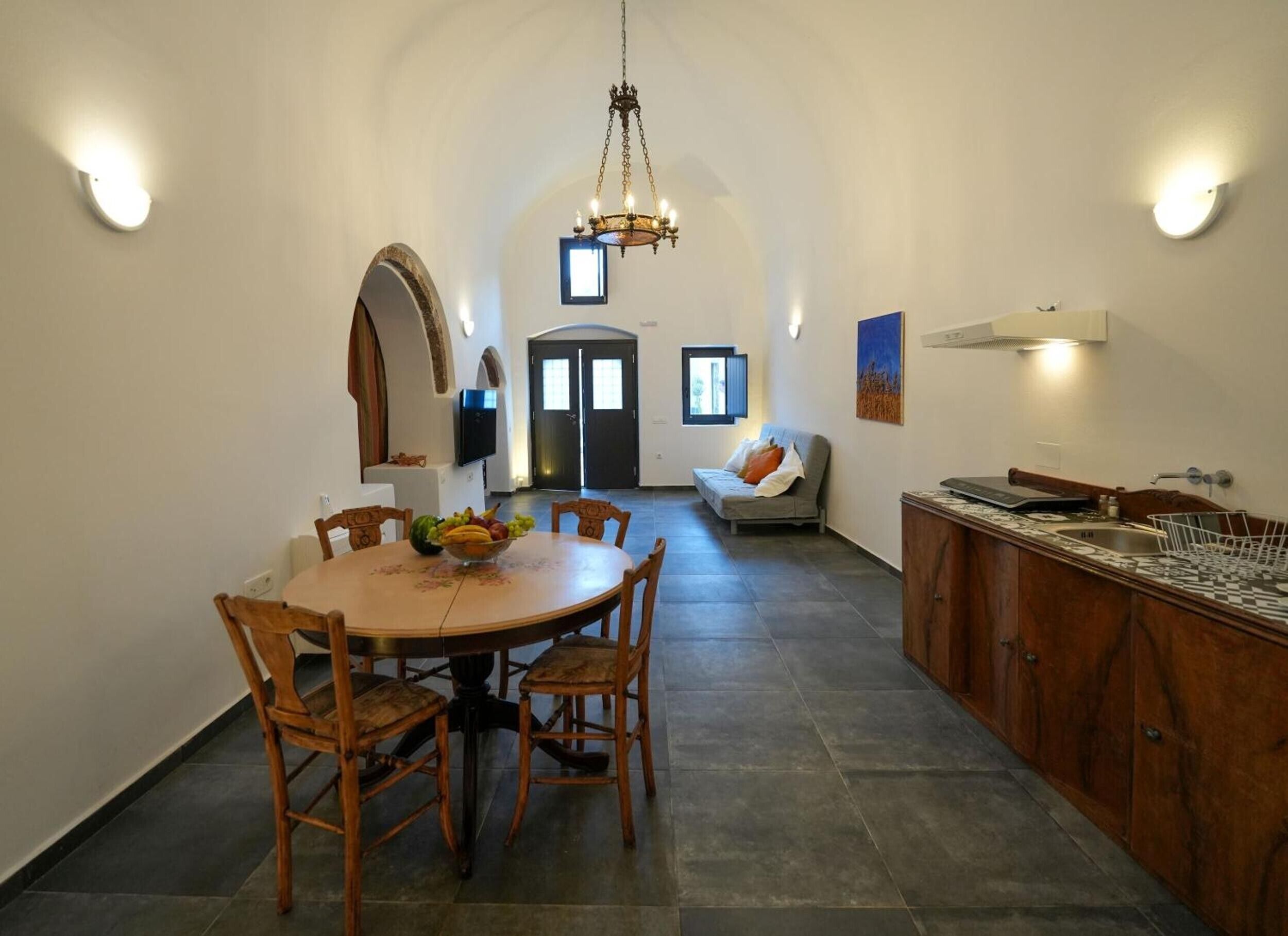 Ein Essbereich mit einem runden Tisch, Stühlen und einer Obstschale. Im Hintergrund befindet sich eine Couch und ein Fernseher.