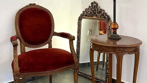 Une pièce avec un fauteuil en velours rouge, une petite table ronde avec une lampe et un tableau accroché au mur.