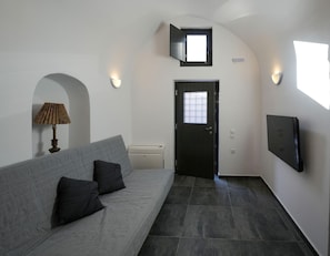 A modern interior with a grey sofa, a flat-screen TV mounted on the wall, and a door with a frosted glass panel. - Apartment 'One-Bedroom' with Wi-Fi and Air Conditioning (Emporio)