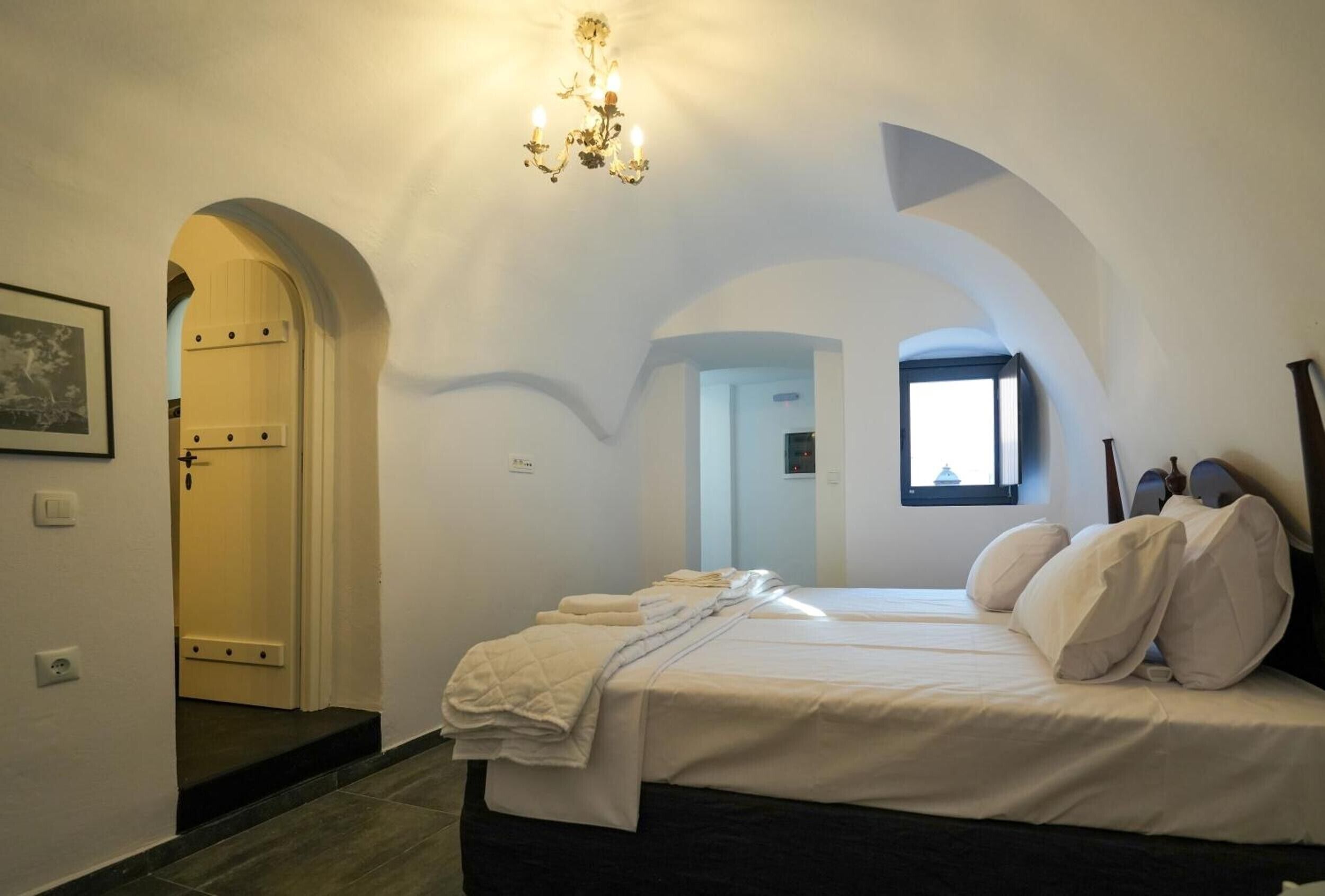 Ein Schlafzimmer mit einem Bett, einer Kandelaber, einem Rundbogen und einem Fenster.