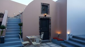 Un petit espace extérieur aménagé avec une table et des chaises, une porte et un escalier menant à l’étage supérieur.