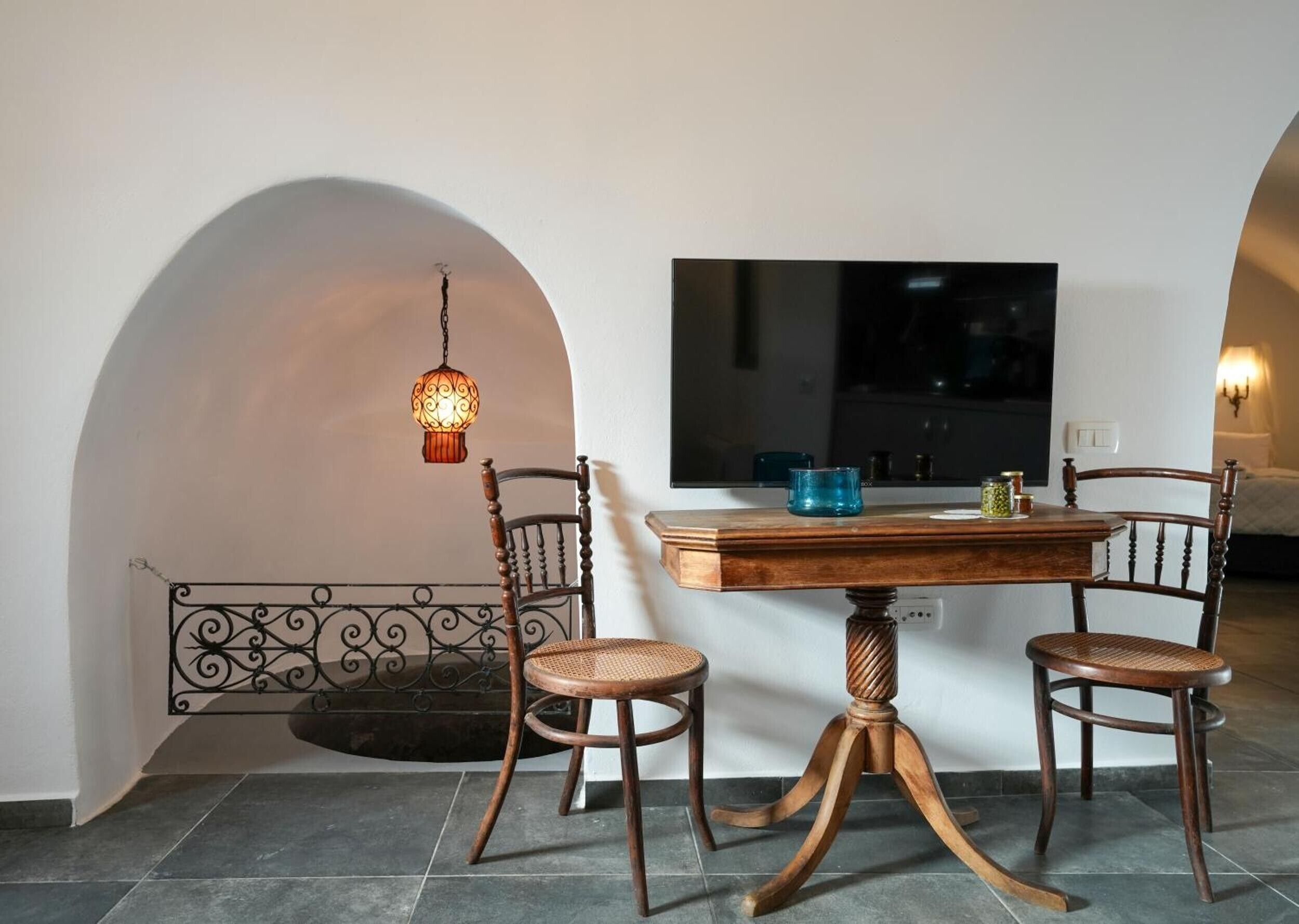 Un comedor con una mesa de madera, dos sillas, una lámpara colgante y un televisor montado en la pared.