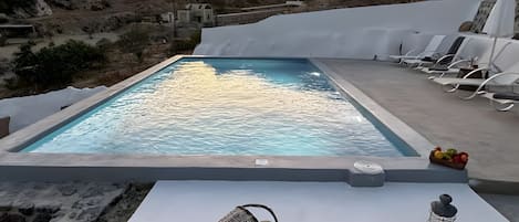 A swimming pool with lounge chairs and a table with a lantern and basket.