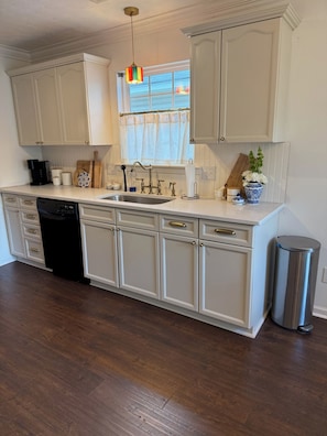 A kitchen with white cabinetry, a stainless steel sink, a dishwasher, and a trash can.