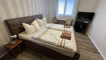 Ein Doppelbett mit gestreifter Bettwäsche, ein Nachttisch mit Lampe, ein Fernseher und ein kleiner Schreibtisch mit Stuhl.