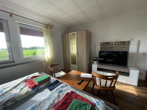 Quarto de hotel com cama, mesa de madeira, televisão e vista para um campo verde.