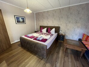 Ein Schlafzimmer mit einem Bett, Nachttischen, einem Hocker und einer Pendelleuchte.