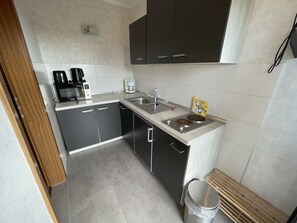 Una cocina compacta con microondas, cafetera y lavamanos.