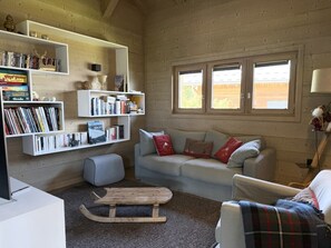 A cozy living room with a sofa, a small table, and bookshelves filled with books. - Chalet Alpa, a chalet with a hot tub (Saint-Gervais-les-Bains)