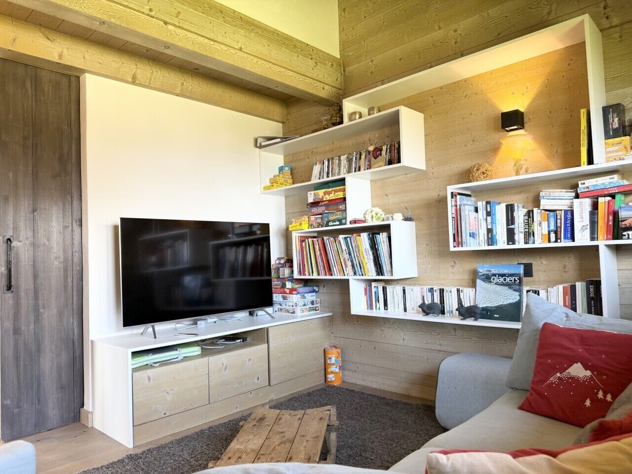 Ein modernes Wohnzimmer mit Flachbildfernseher, integrierten Bücherregalen, einem grauen Sofa und einem Holztisch.