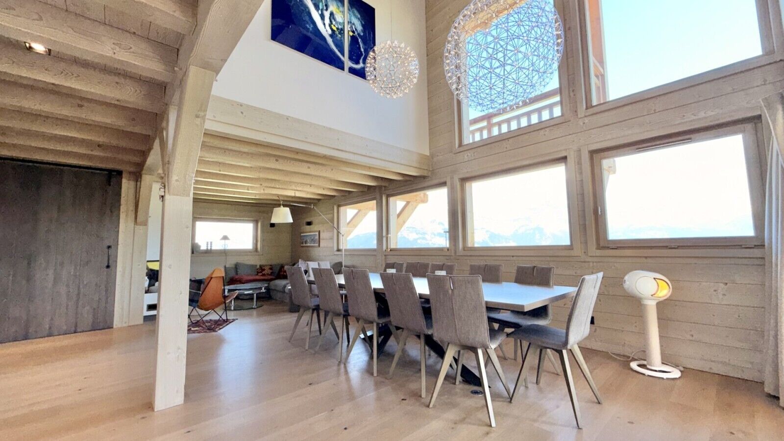 Un vaste espace dédié à la salle à manger, avec une longue table et des chaises, de grandes fenêtres et un plafond haut avec des poutres apparentes.