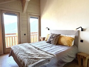 A bedroom with a bed, a wooden headboard, a nightstand, a small wooden stool, and a view of the outdoors through a door. - Chalet Alpa, a chalet with a hot tub (Saint-Gervais-les-Bains)