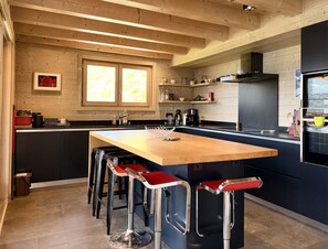 A modern kitchen with a central island, bar stools, and wooden beams on the ceiling. - Chalet Alpa, a chalet with a hot tub (Saint-Gervais-les-Bains)