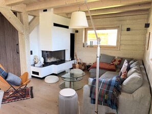 A cozy living room with a fireplace, a sofa, a round glass table, and a hanging light fixture. - Alpa Cabin (12 People) View of Mont Blanc & Jacuzzi (Saint-Gervais-les-Bains)