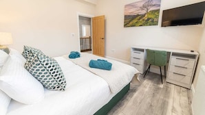 Een slaapkamer met een bed, een bureau, een stoel, een televisie en een schilderij aan de muur.