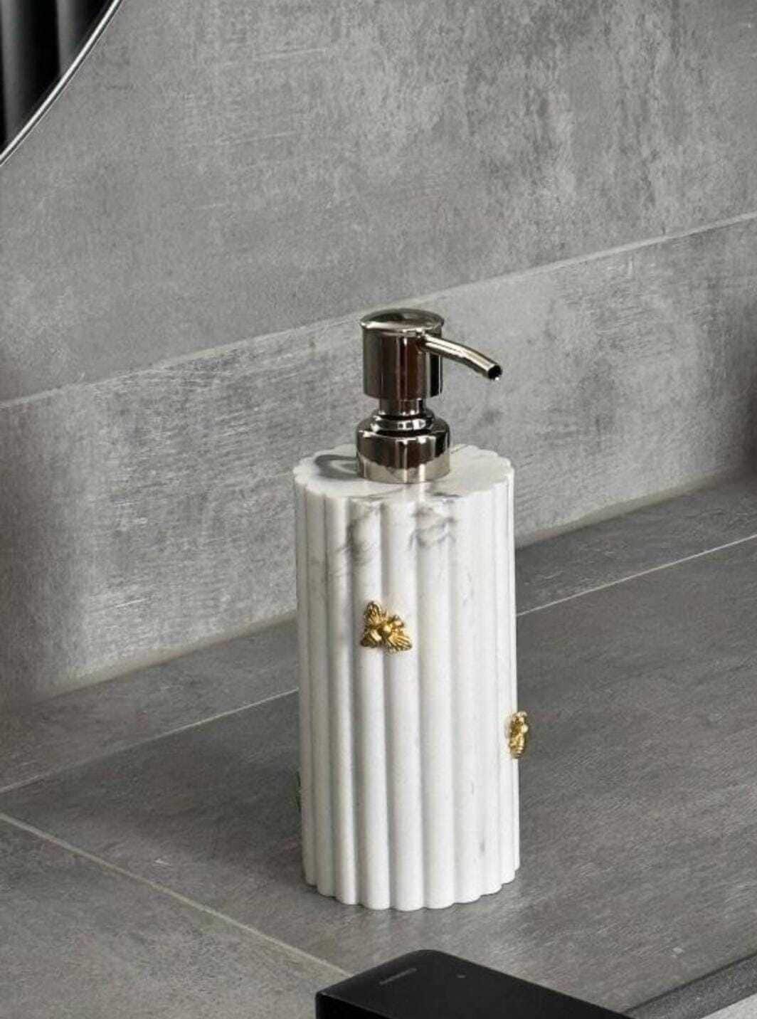 A white, cylindrical dispenser with a metallic pump, placed on a grey tiled surface.