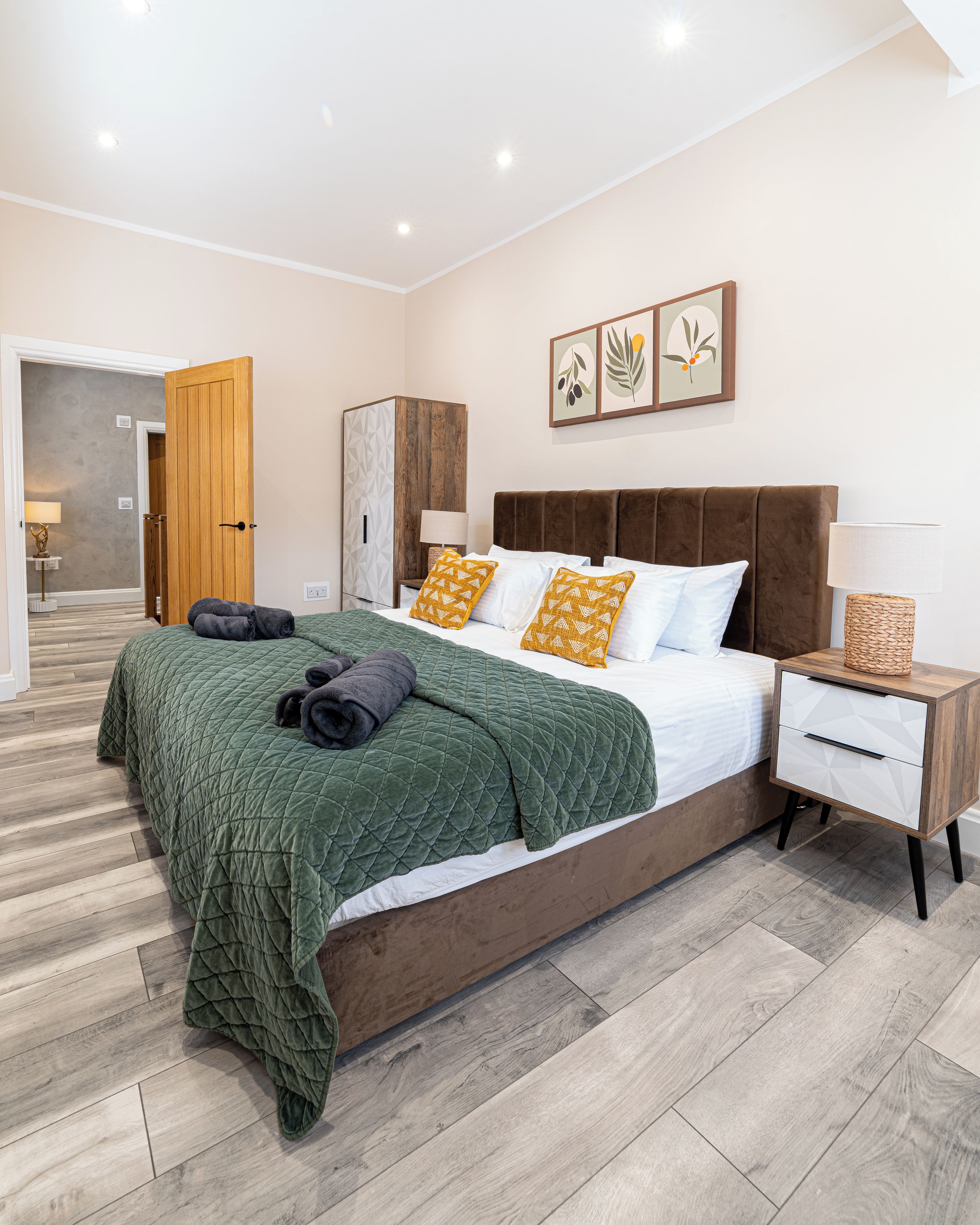 A modern bedroom with a large bed, a wooden wardrobe, a nightstand, and a wall-mounted lamp.