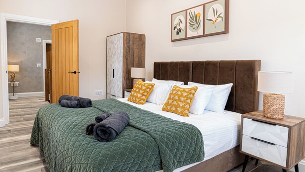 Een moderne slaapkamer met een groot bed, een houten garderobe, een nachtkastje en een wandlamp.
