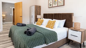 A modern bedroom with a large bed, a wooden wardrobe, a nightstand, and a wall-mounted lamp.