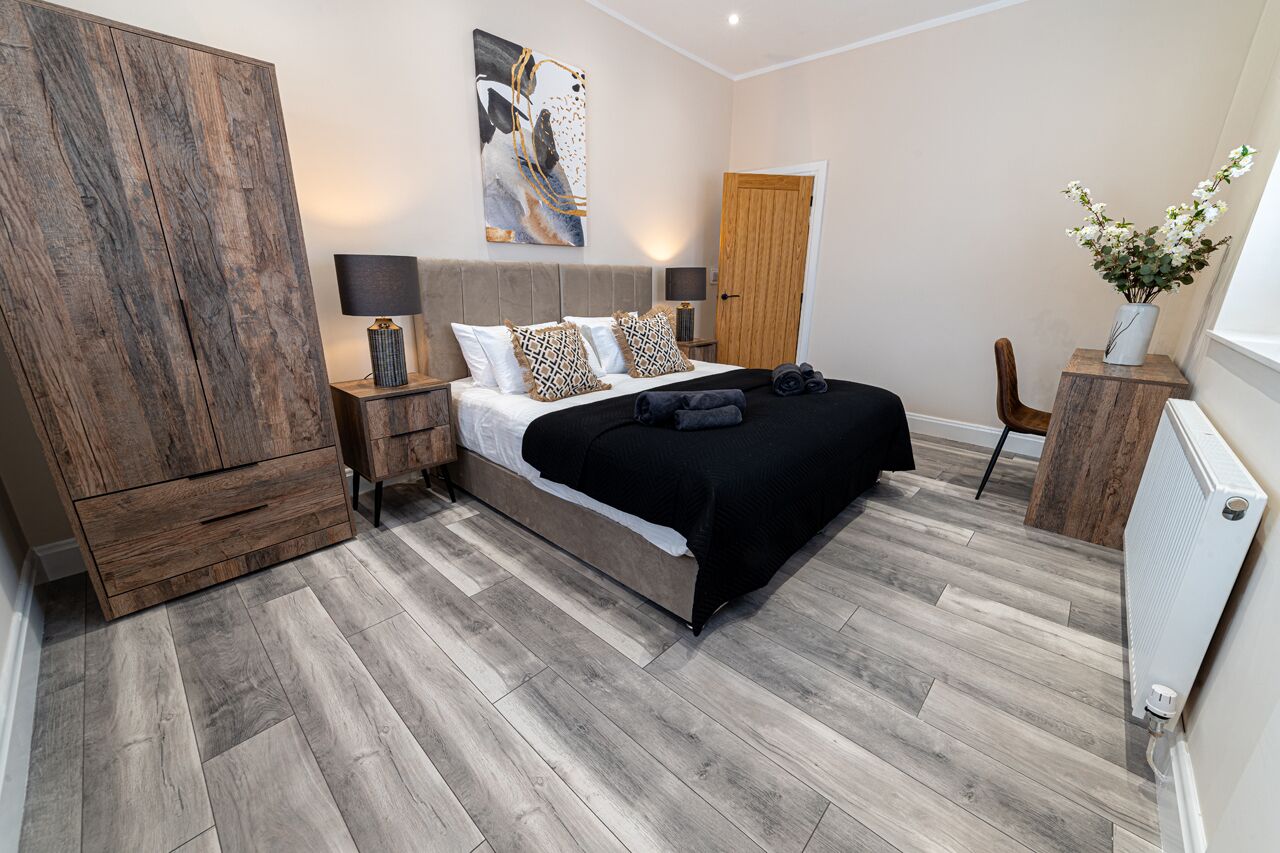 Quarto moderno com cama grande, guarda-roupa de madeira, abajures e um painel decorativo na parede.