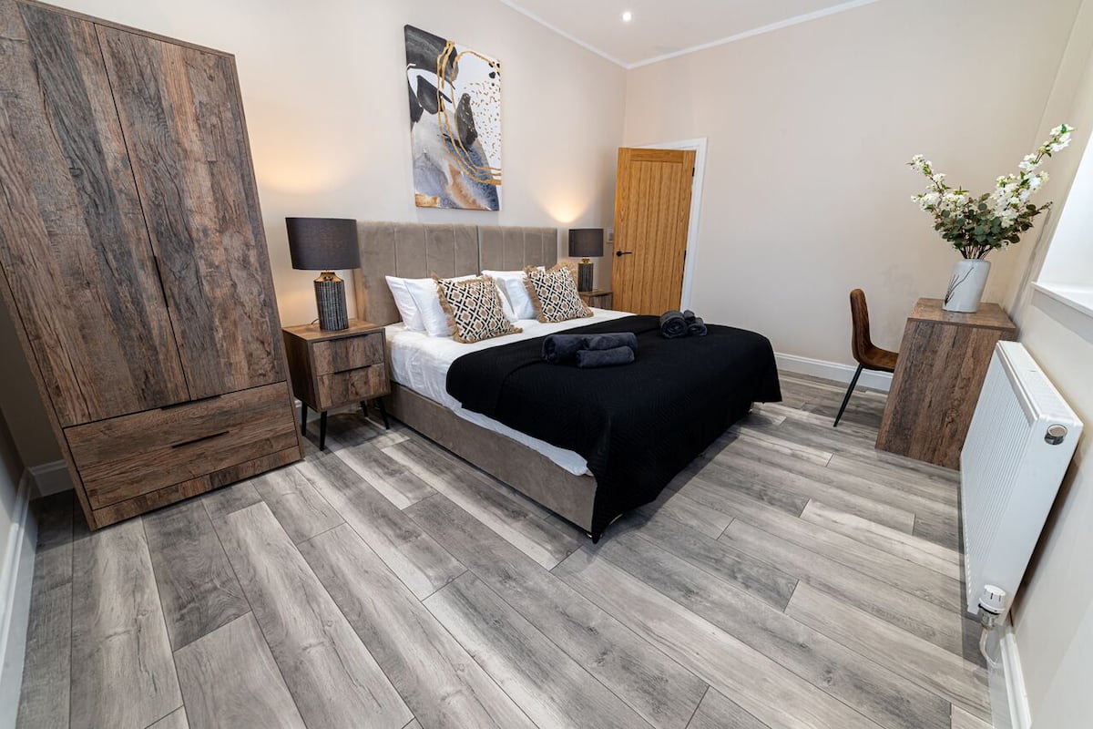 A modern bedroom with a large bed, wooden wardrobe, bedside lamps, and a decorative wall piece.