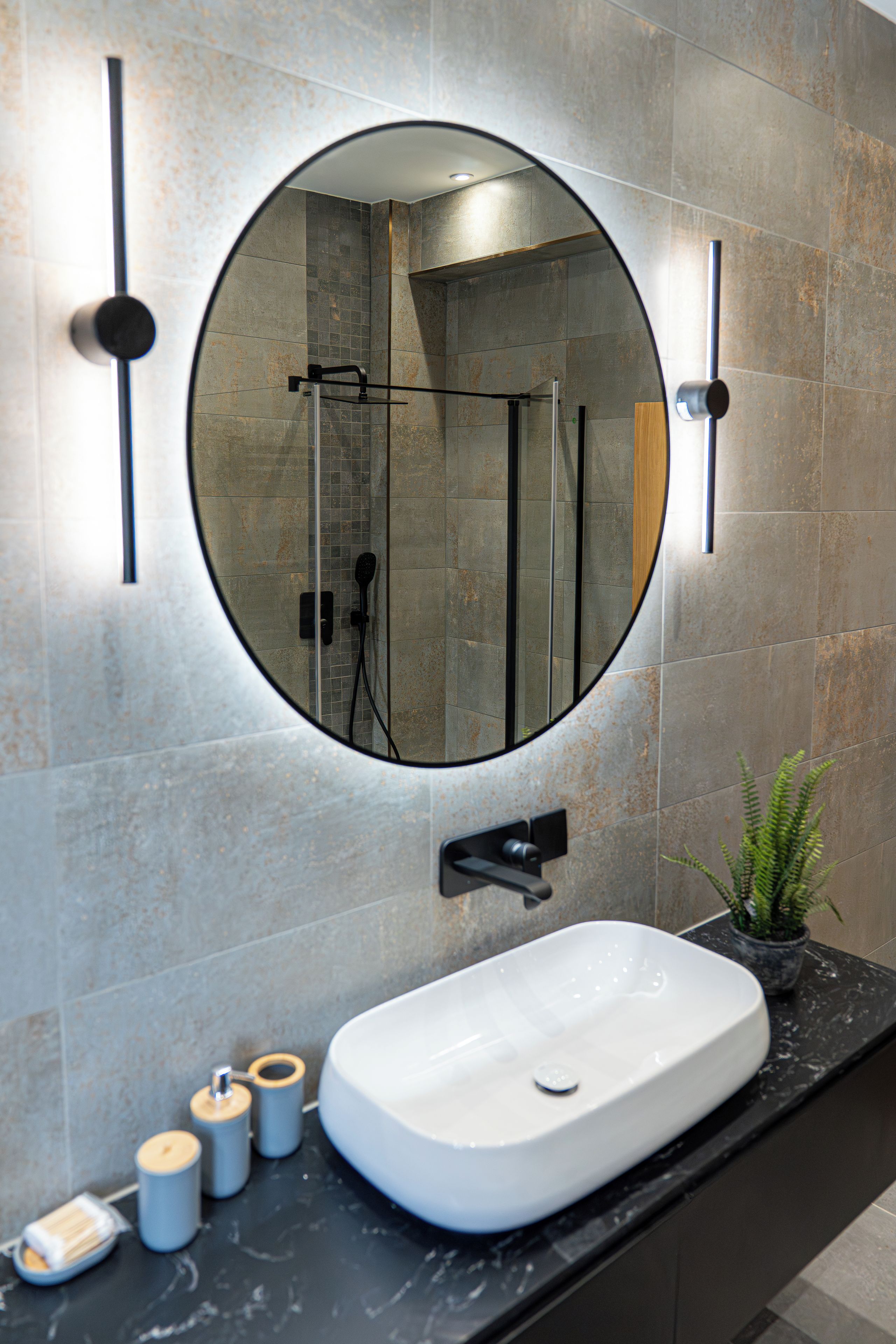 A bathroom with a round mirror, a white sink, and a shower area.