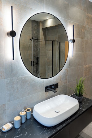 Un baño con un espejo redondo, un lavabo blanco y una zona de ducha.