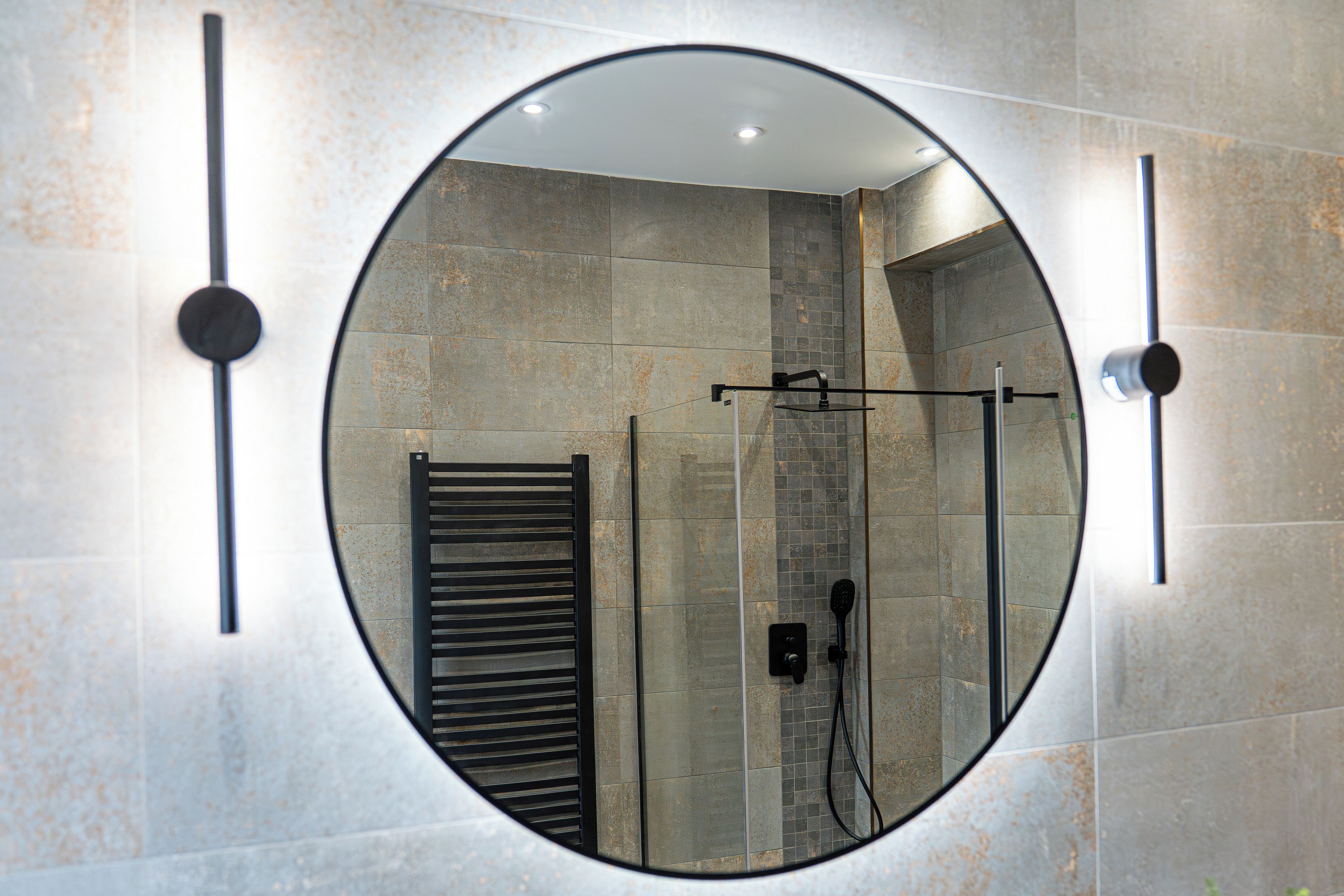 A bathroom with a round mirror, a towel rack, and a shower area.