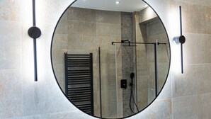 Een badkamer met een ronde spiegel, een handdoekhouder en een douchehoek.