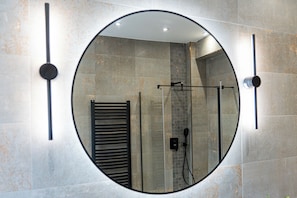 A bathroom with a round mirror, a towel rack, and a shower area.