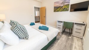 Een slaapkamer met een bed, een bureau, een stoel, een televisie en een schilderij aan de muur.