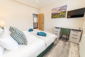 Quarto com cama, escrivaninha, cadeira, televisão e um quadro na parede.