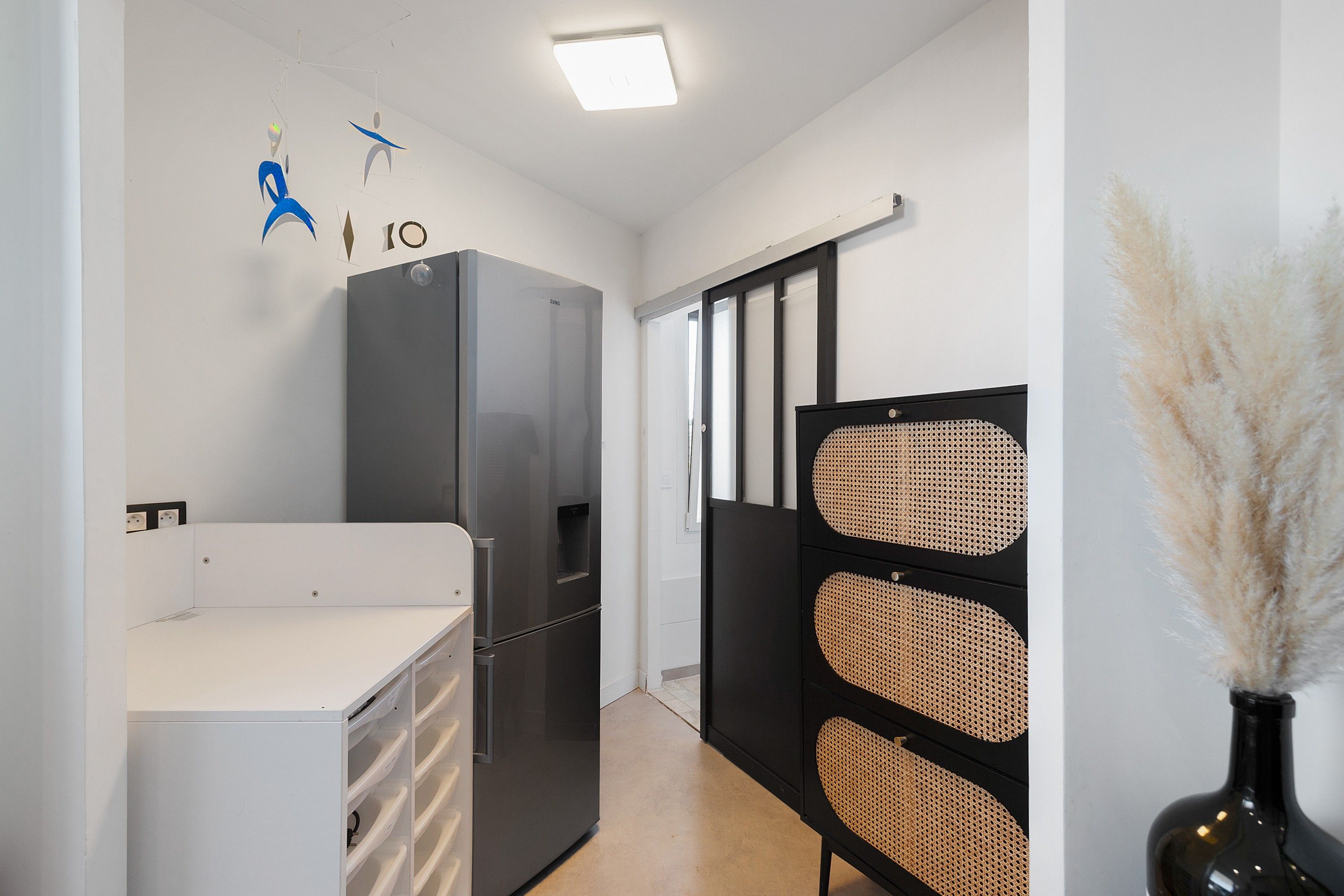 A compact kitchen with a refrigerator, a white countertop, and a black cabinet with woven panels.