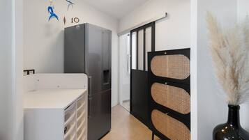 A compact kitchen with a refrigerator, a white countertop, and a black cabinet with woven panels.