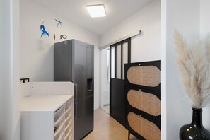 Una cocina compacta con refrigerador, encimera blanca y un mueble negro con paneles trenzados.